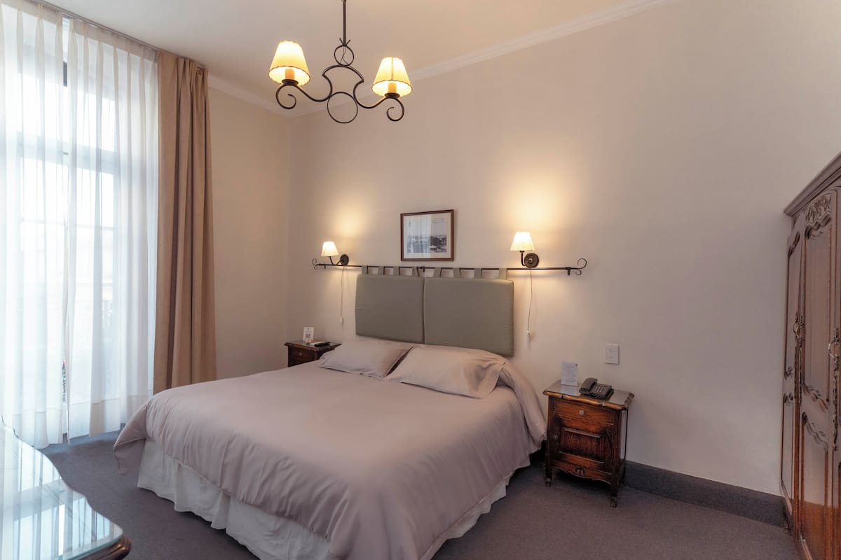 Habitación de hotel ordenada con una cama grande, mesitas de noche, un escritorio y un armario.