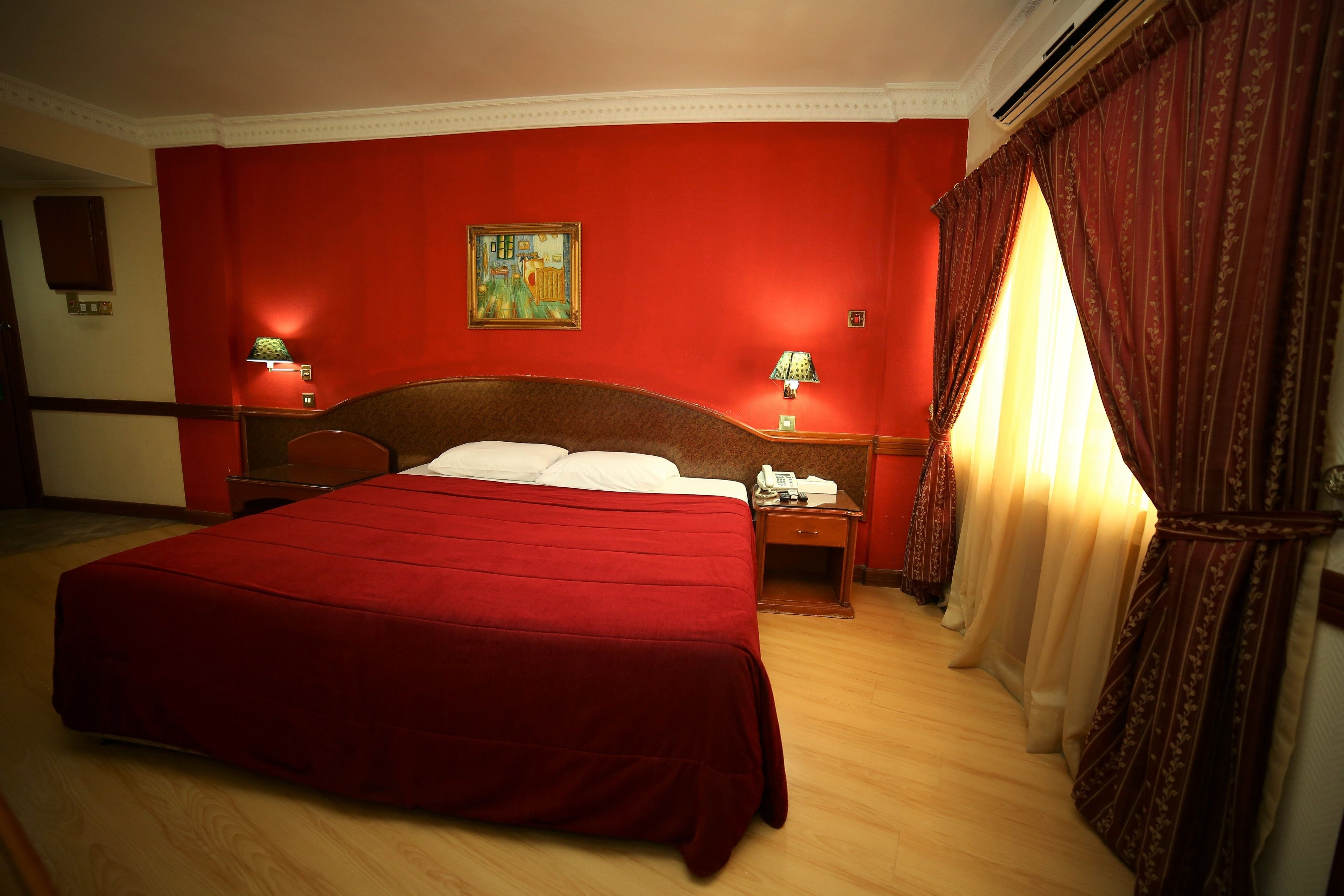 A hotel room with a large bed, red walls, and two bedside lamps.