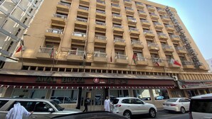 Un hotel de varios pisos con balcones, un restaurante a nivel de calle y varios coches aparcados delante.