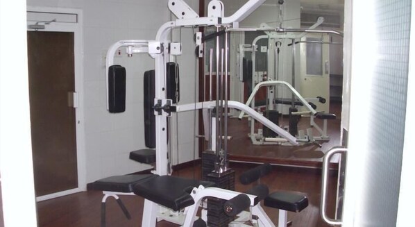 A gym with various exercise machines, a bench, and a mirror on the wall.