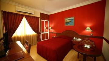 Una habitación de hotel con una cama, un escritorio, una silla, una mesita y un cuadro en la pared.