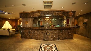 Zona de recepción de hotel con mostrador de mármol, relojes y un mostrador de atención al cliente.