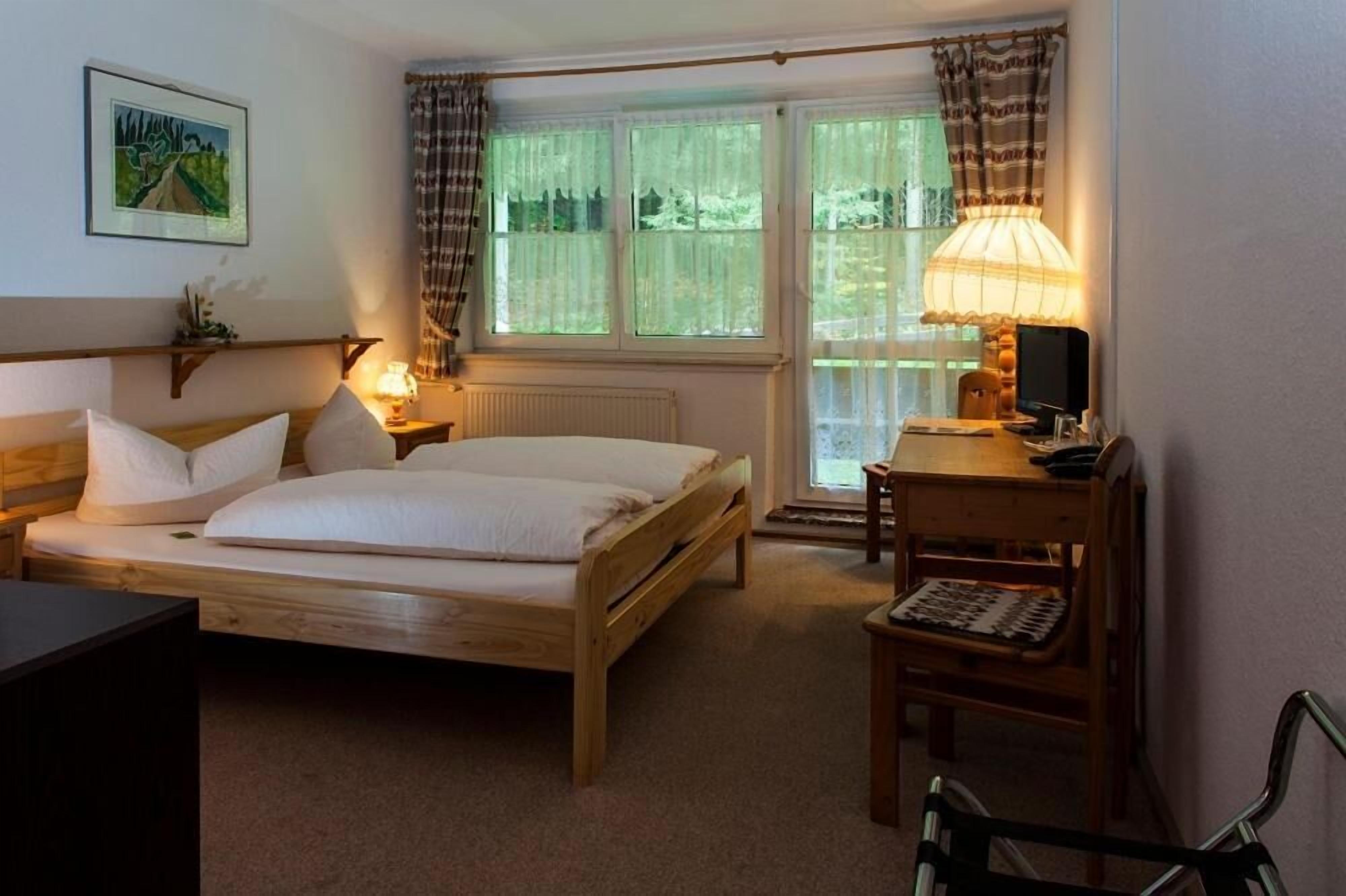 Una habitación con una cama de madera, un escritorio con lámpara y una ventana con cortinas.