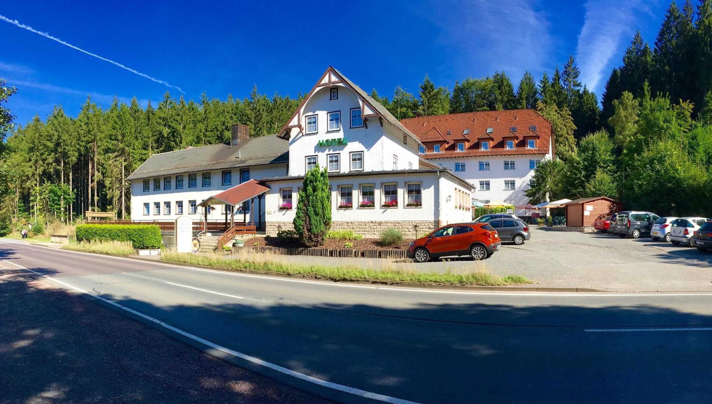 Ein zweistöckiges Hotel mit weißer Fassade, rotem Dach und einem Parkplatz mit mehreren Autos.