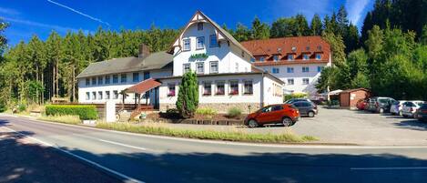 A two-story hotel with a white facade, a red roof, and a parking lot with several cars.