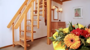 Una escalera de madera en una habitación con un aparador de madera y un arreglo floral en el suelo.
