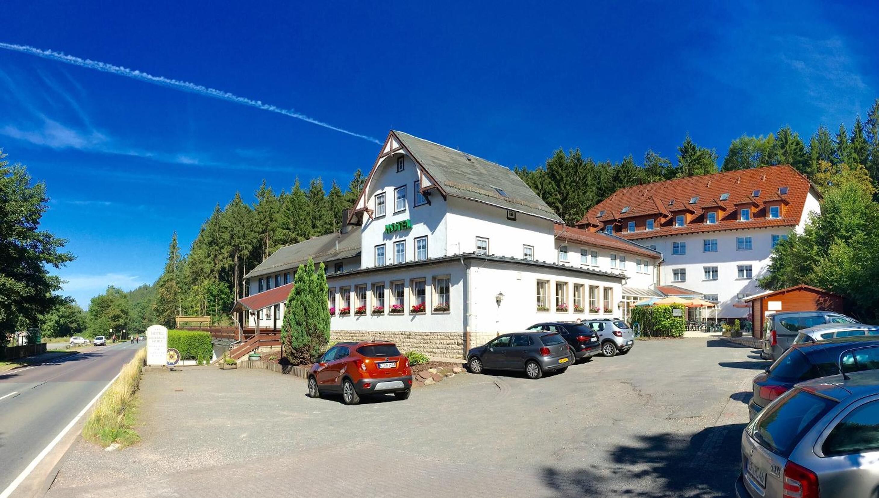 A hotel with a white facade, multiple windows, and a parking lot with several cars.