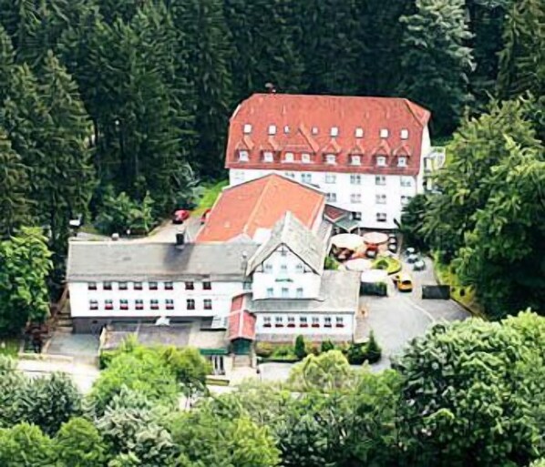 A large building with a red roof, surrounded by dense greenery.