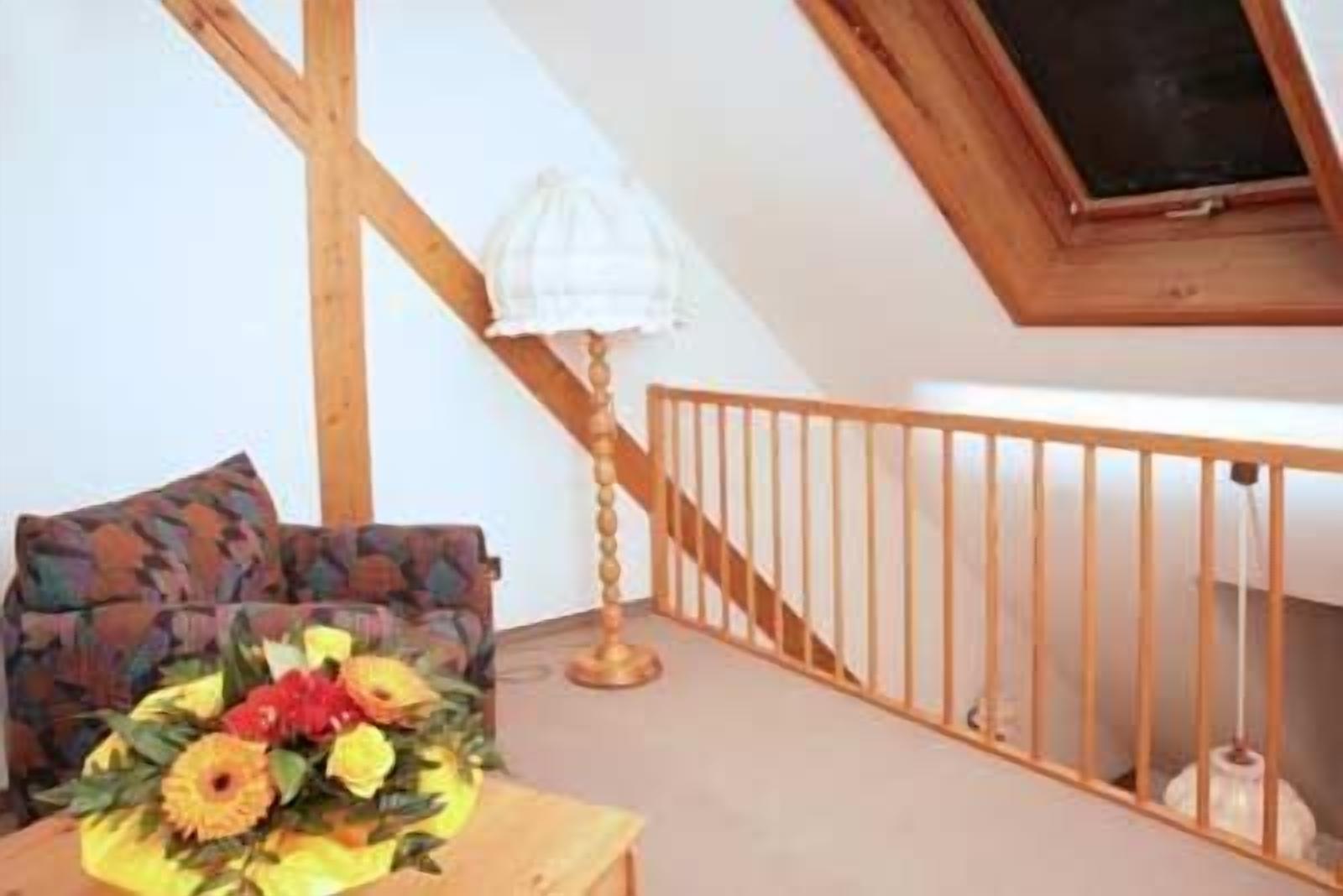 A room with a wooden staircase, a wooden railing, and a table with a floral arrangement.