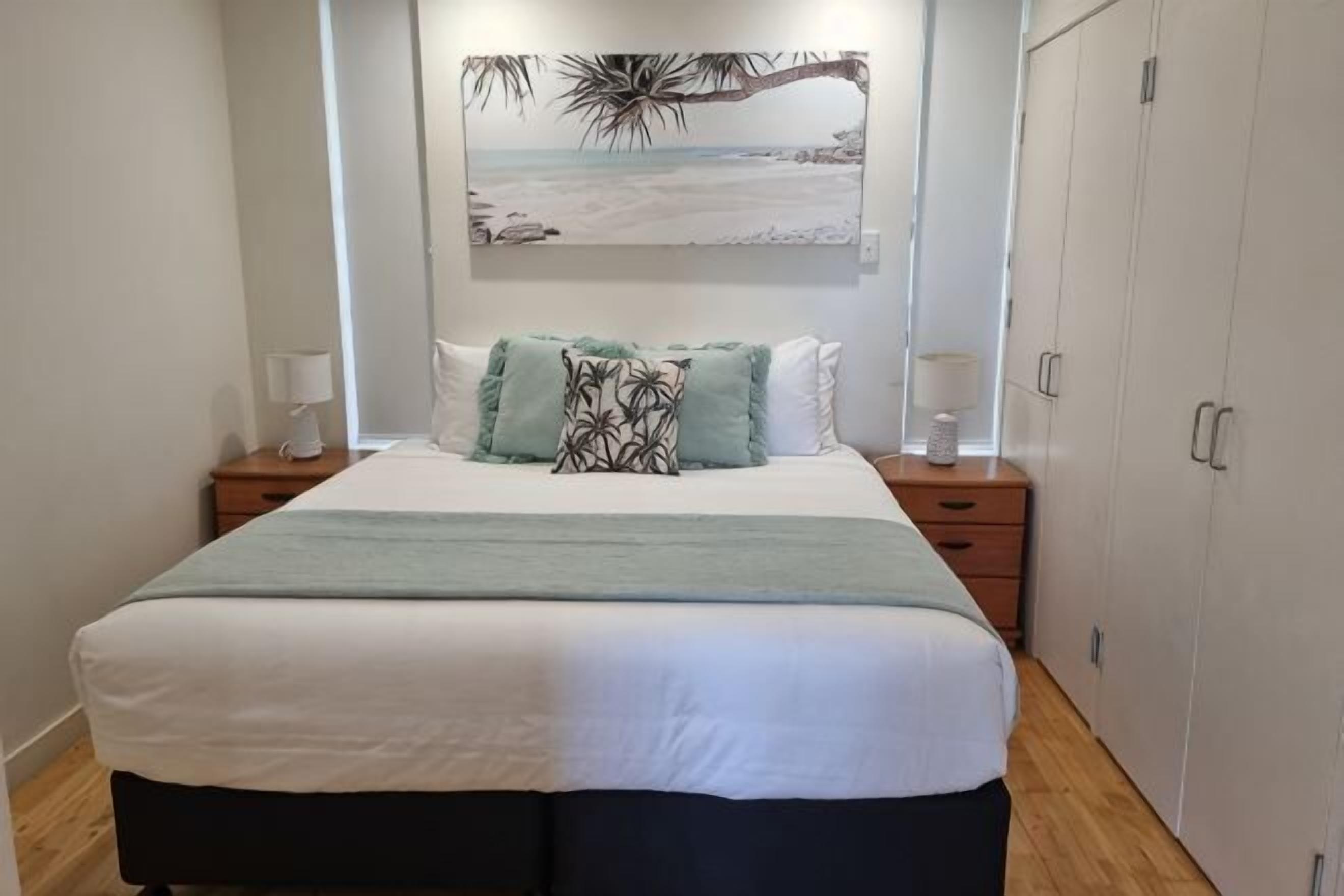 A bedroom with a bed, nightstands, a wardrobe, and a beach-themed painting on the wall.