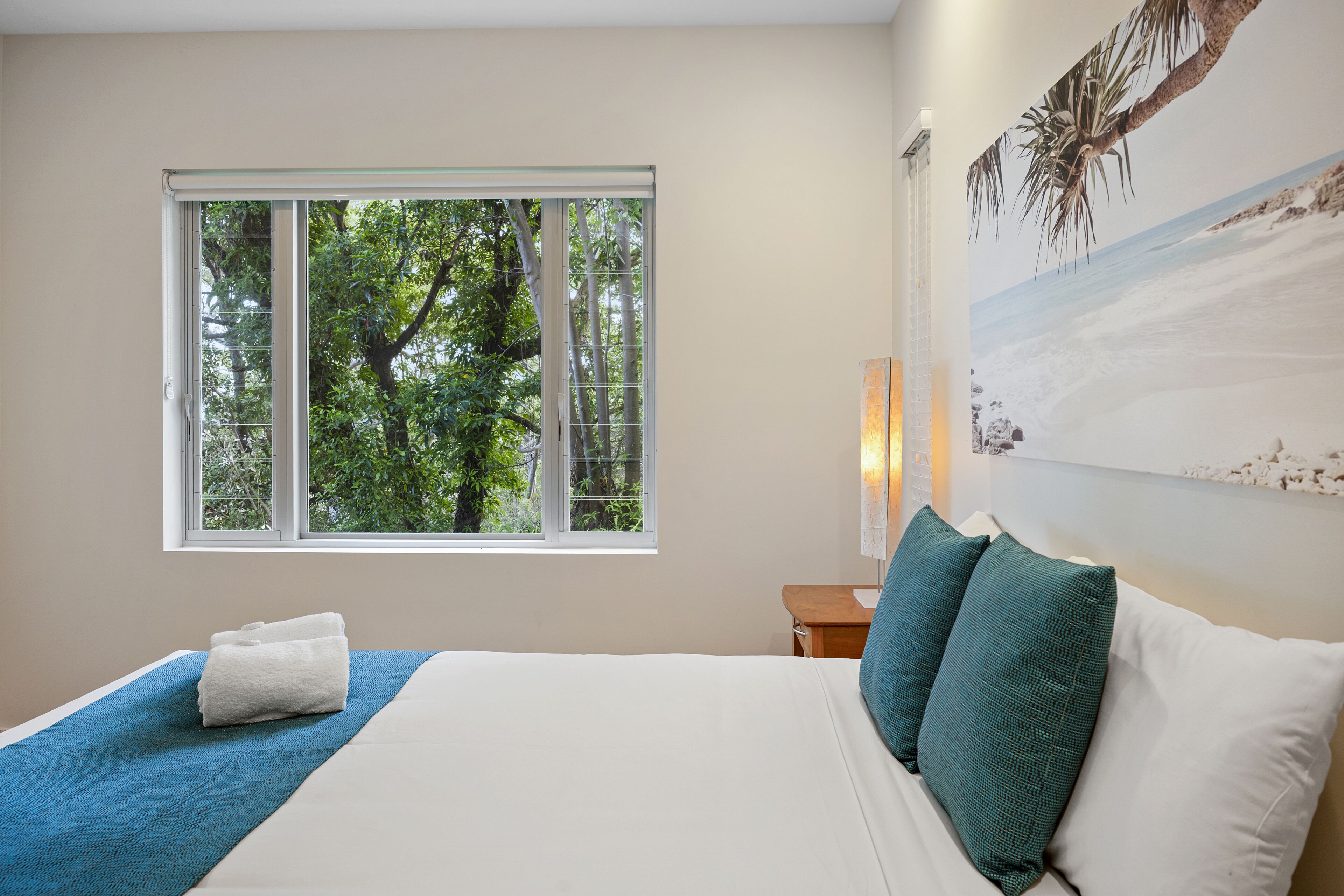Una camera da letto con un letto grande, una finestra vista alberi e una lampada a parete.