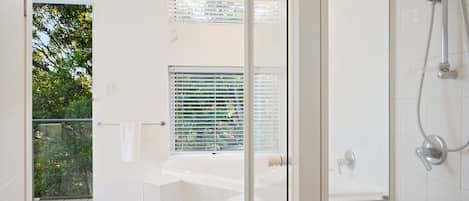 A modern bathroom with a glass shower enclosure, a large bathtub, and a window with blinds.