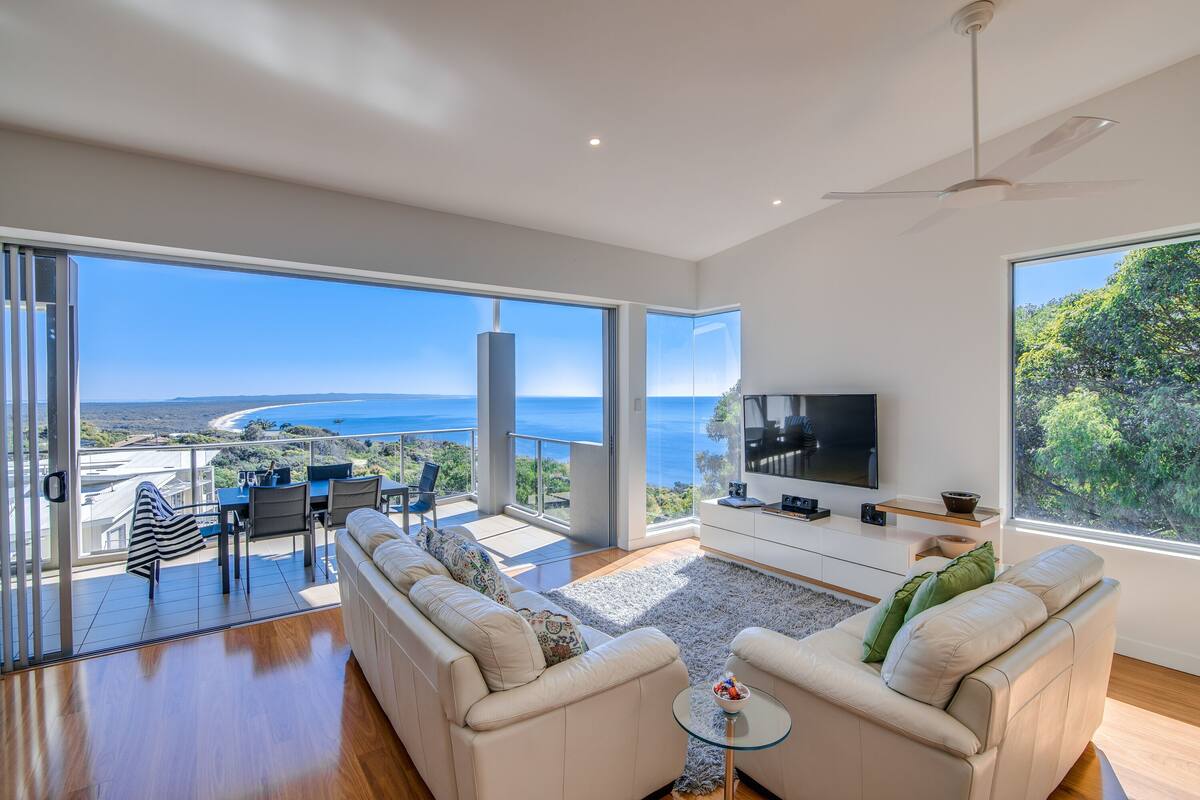 Un salón amplio con televisor grande, asientos cómodos y un balcón con vistas al mar.