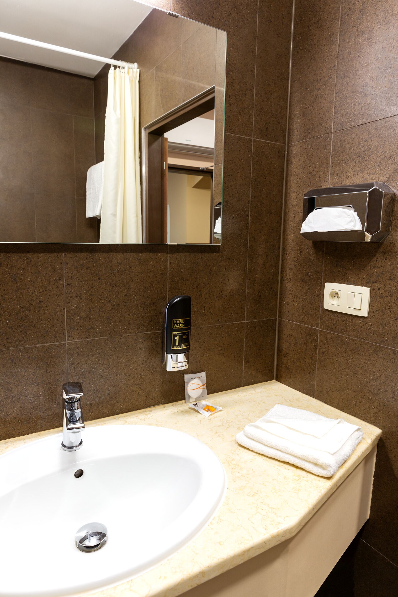 Une salle de bain équipée d’un lavabo, d’un miroir, d’un distributeur de serviettes et d’un sèche-mains.