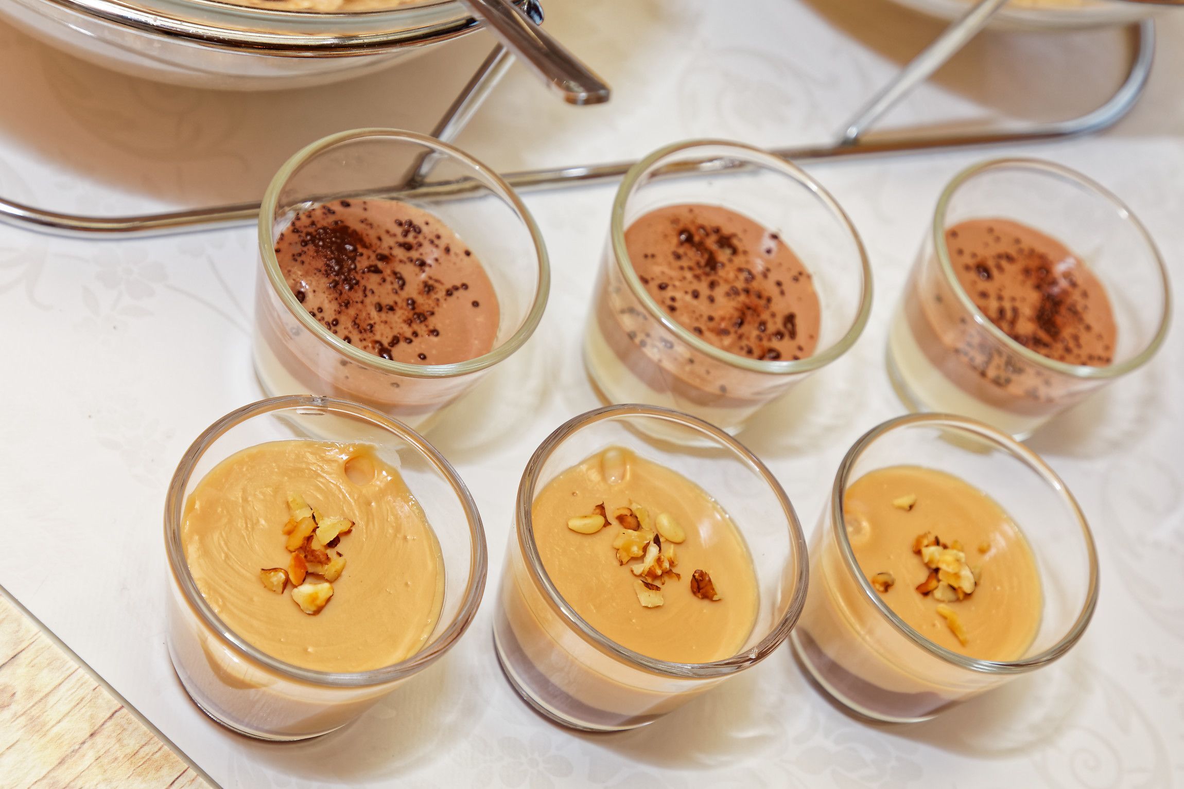 Cuatro copas de vidrio con postre sobre un mantel blanco estampado con motivos florales.
