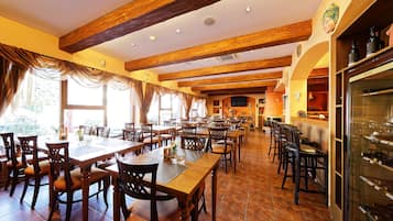 A spacious restaurant with wooden beams, large windows, and a wine refrigerator.