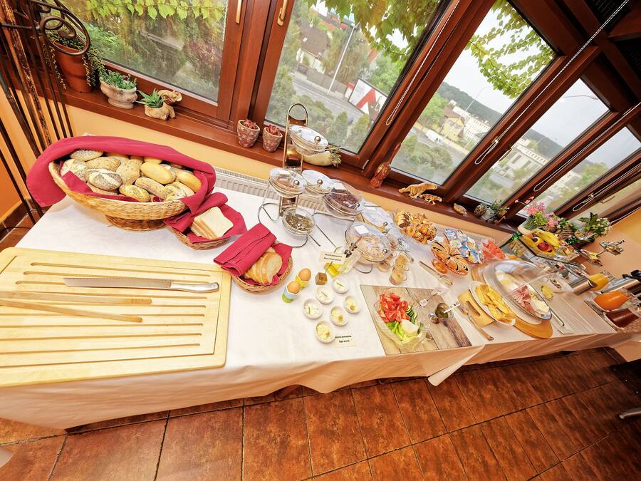 A buffet table with various food items and utensils, set against a window with a view of buildings and greenery.