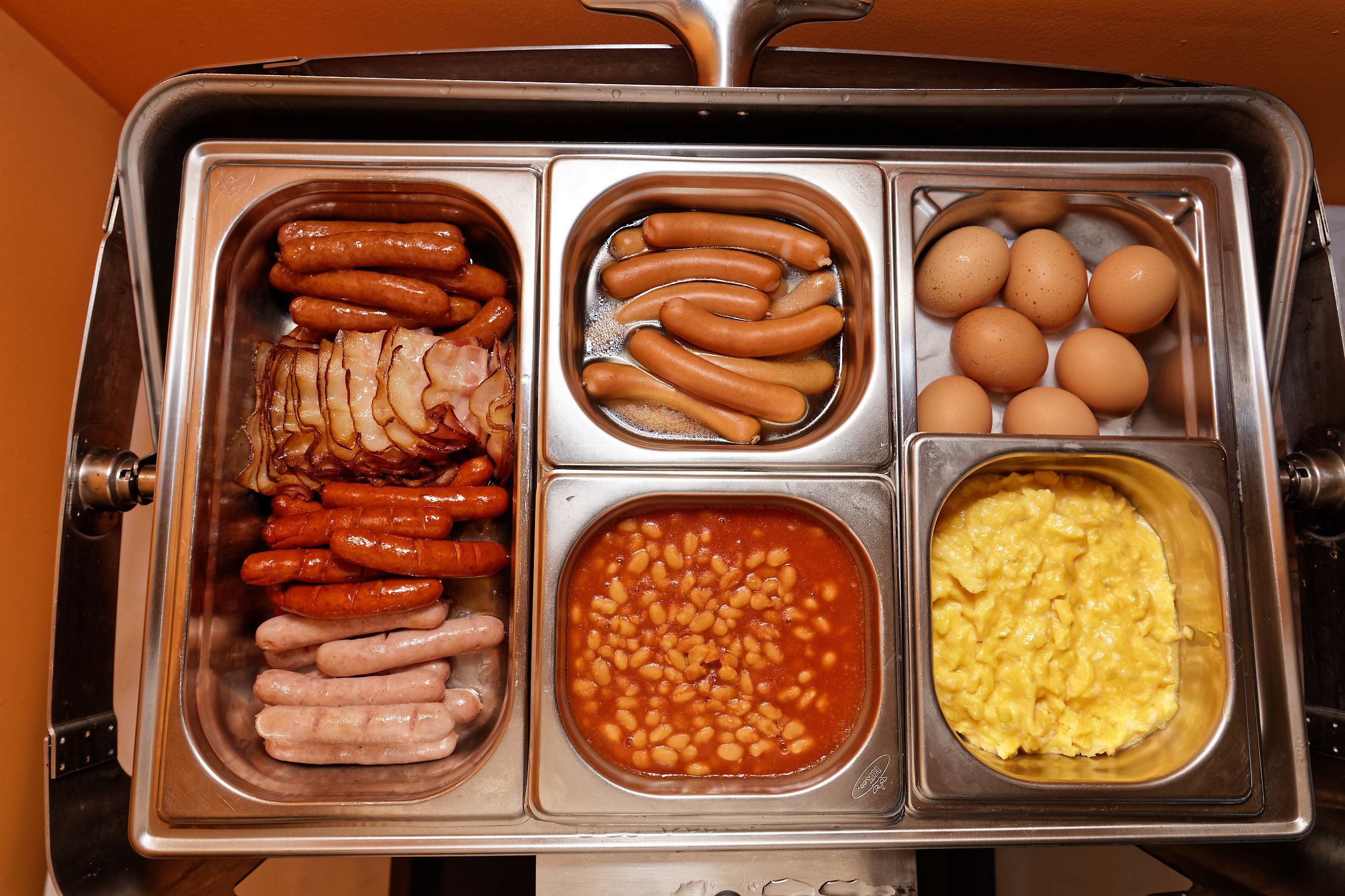 A buffet with various food options including sausages, eggs, beans, and scrambled eggs.