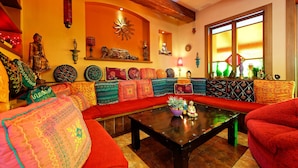 Un salón acogedor con techo de madera, cojines coloridos, una mesa de centro con objetos decorativos y un amplio ventanal con vistas.