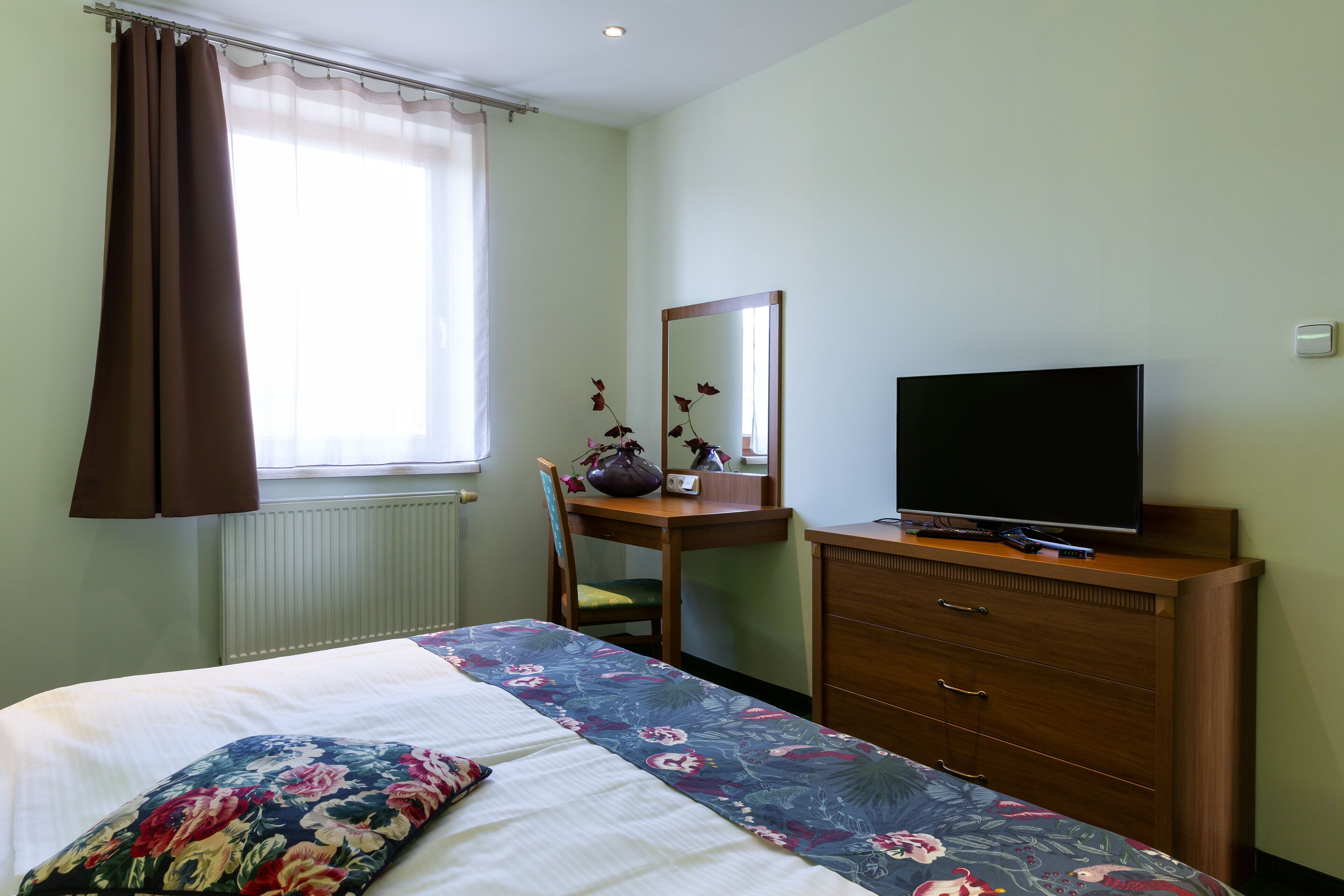 Un dormitorio con cama, cómoda, televisor y ventana con cortinas.