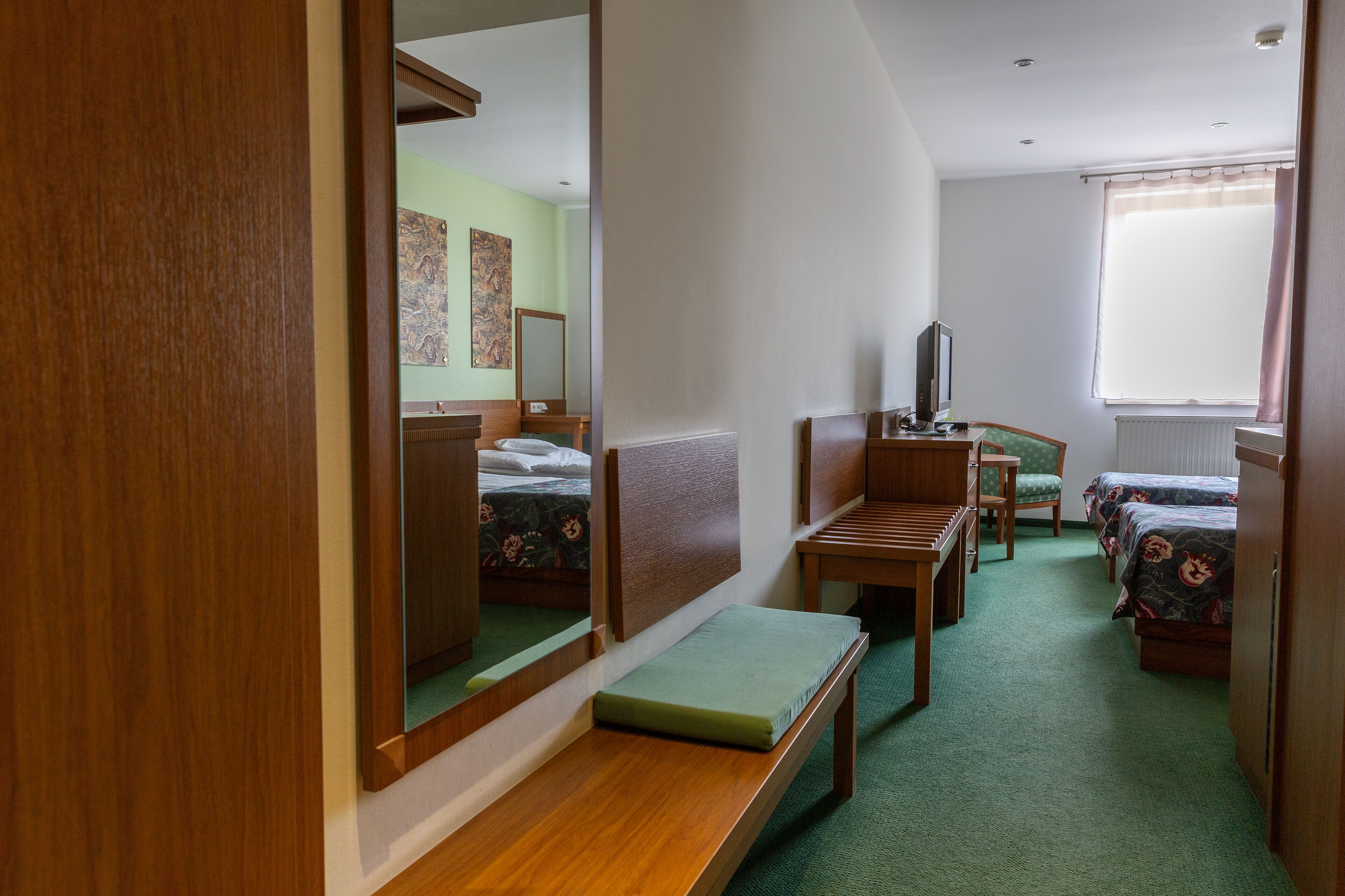 A hotel room with a bed, a desk, a chair, a mirror, and a window.