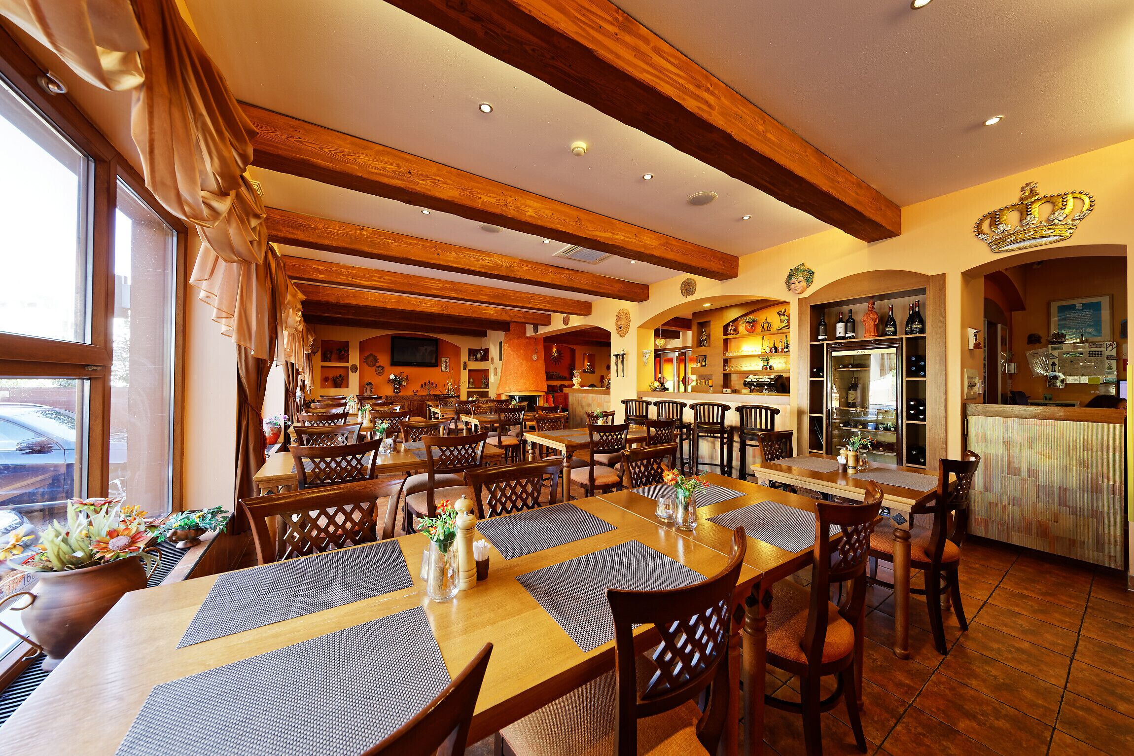 Restaurante com vigas de madeira, mesas com jogos americanos e área de bar com decoração em forma de coroa.