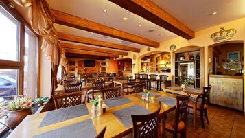 Restaurante com vigas de madeira, mesas com jogos americanos e área de bar com decoração em forma de coroa.