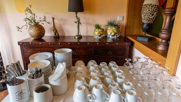 Una mesa con tazas de cerámica blanca y cristalería, un aparador de madera con adornos y una lámpara.