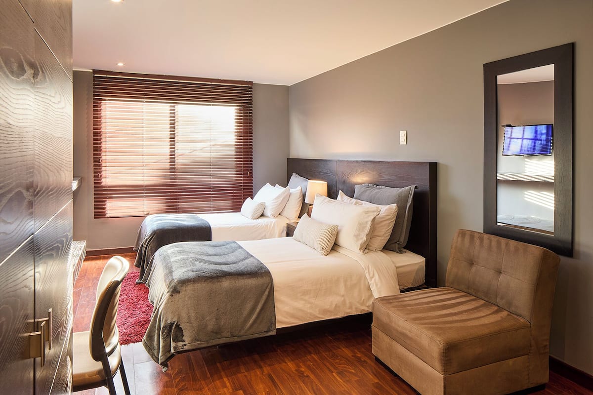 Quarto moderno com uma cama grande, um sofá e uma televisão fixada na parede.