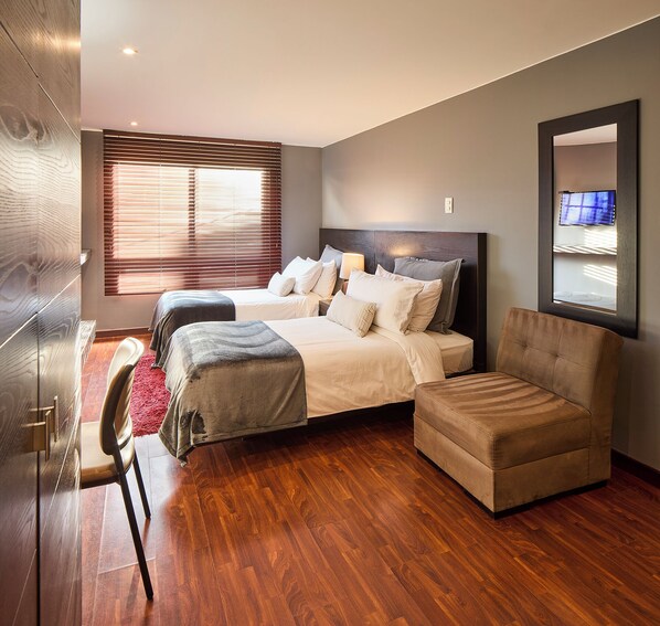 A modern bedroom with a large bed, a sofa, and a TV mounted on the wall. - Nico ApartaSuites (Bogotá)