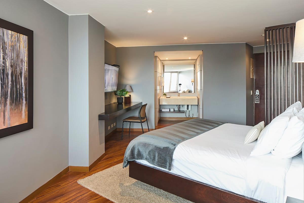 Quarto moderno com uma cama grande, uma escrivaninha com cadeira, uma toucador com espelho e um quadro na parede.