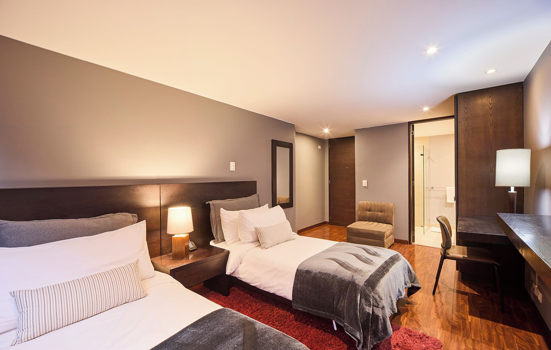 Habitación de hotel con dos camas, un escritorio, una silla, un espejo y zona de ducha.