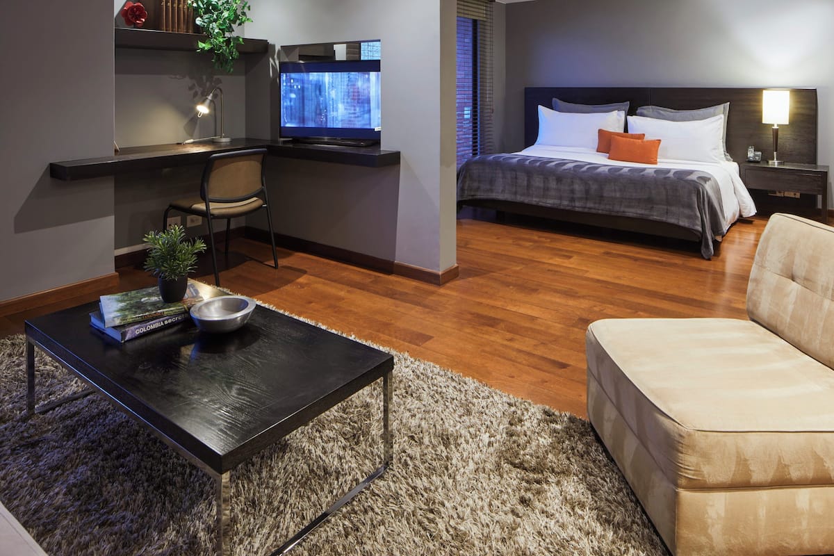 Quarto de hotel moderno com cama, escrivaninha com computador, sofá e mesa de centro.