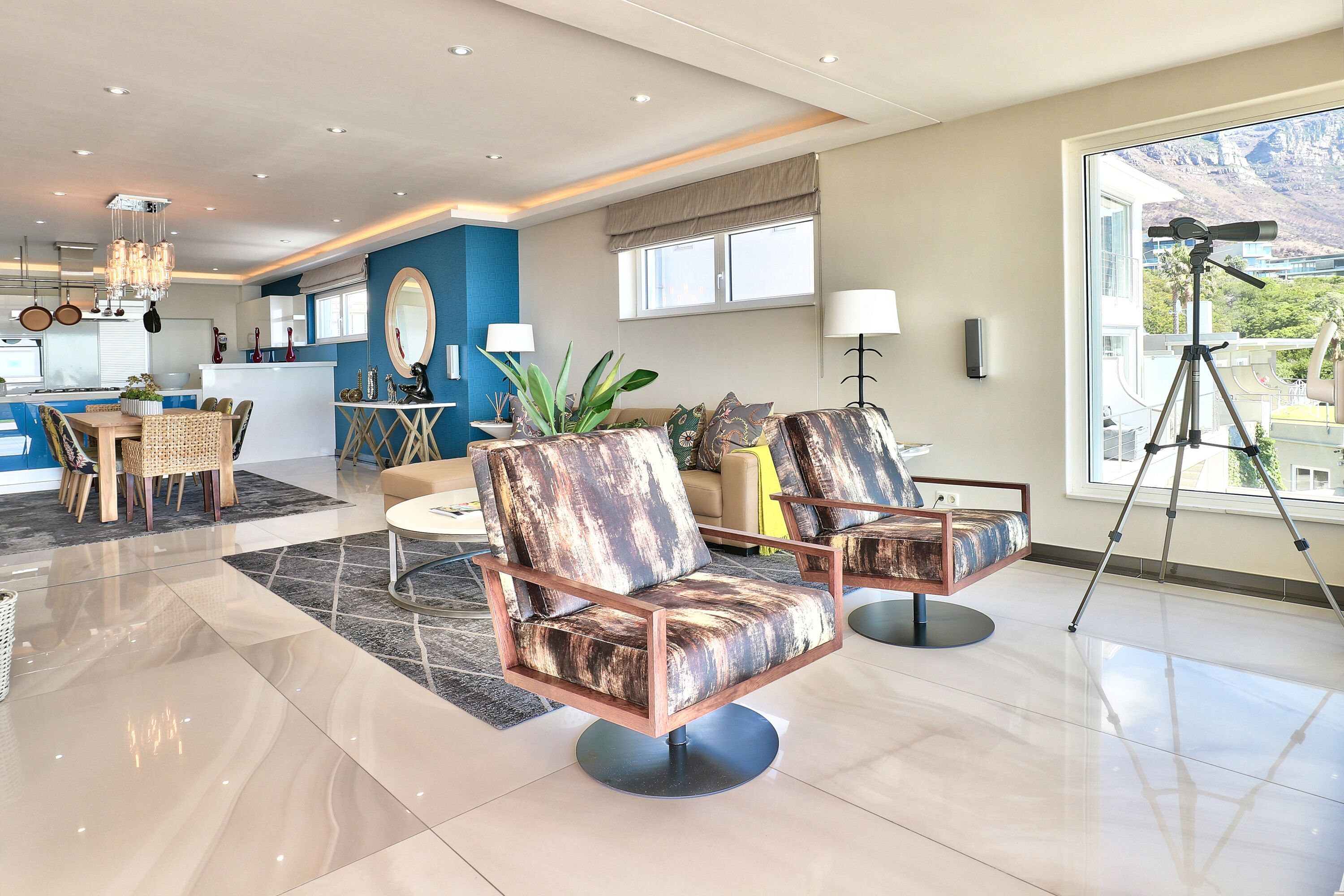 A modern living room with a large window, a dining area, and a kitchen.