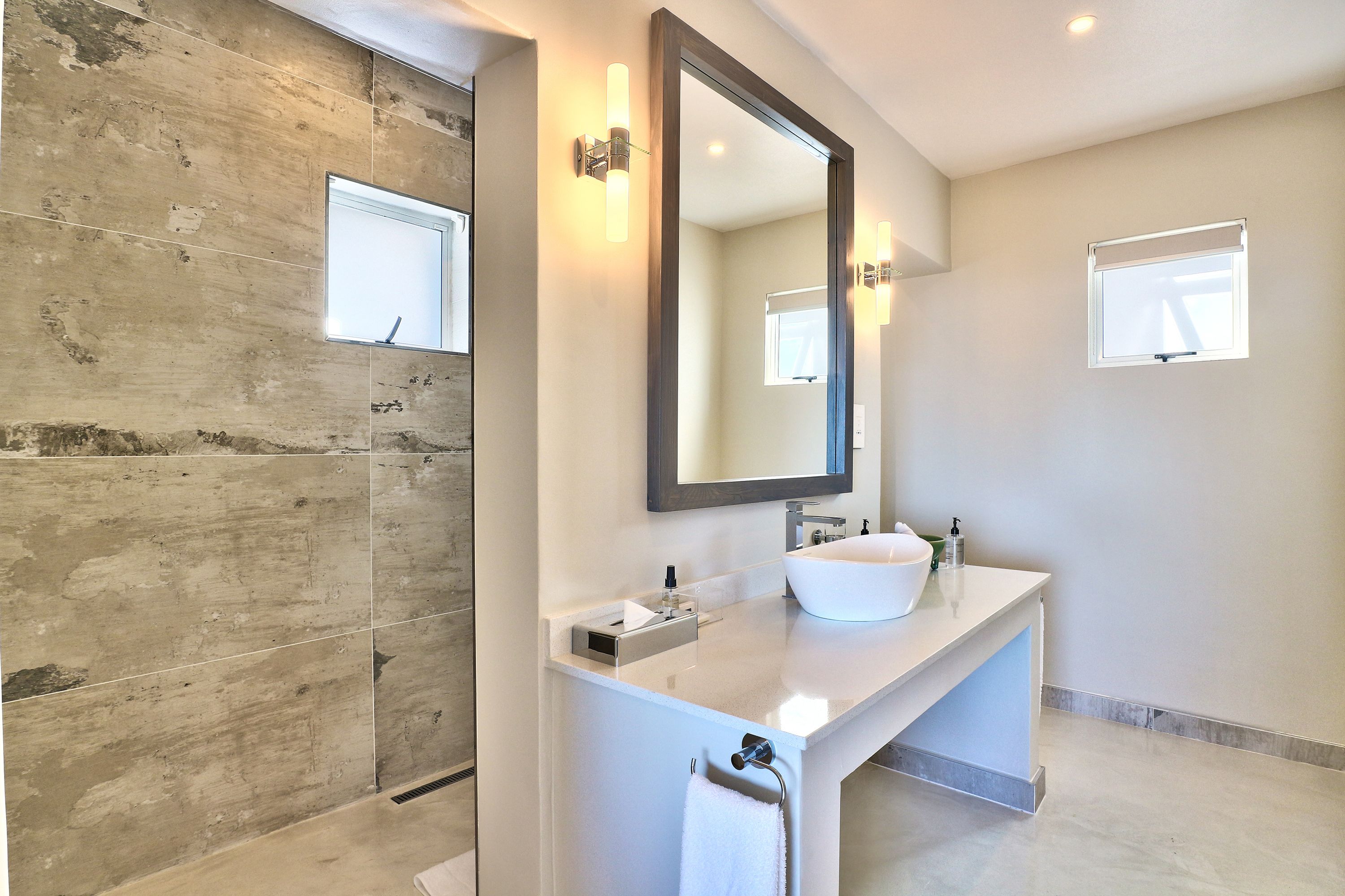 A modern bathroom with a large mirror, a white sink, and a towel rack.