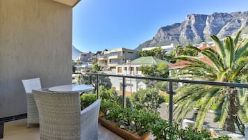 A balcony with wicker furniture, a view of buildings, and a mountain in the background.