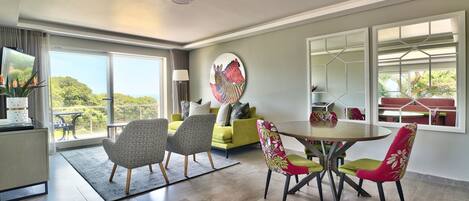 A modern living room with a dining area, large windows, and a view of greenery.
