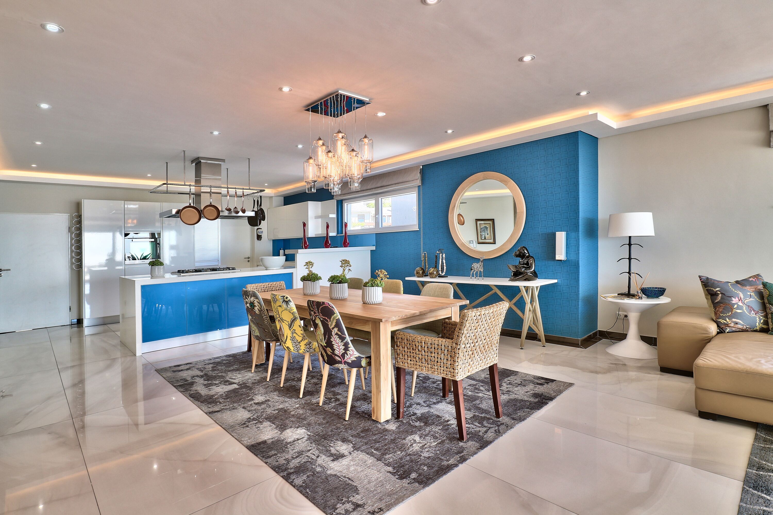 Una cocina moderna con una isla central, comedor con candelabro y sala de estar con sofá y lámpara.