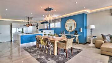 Una cocina moderna con una isla central, comedor con candelabro y sala de estar con sofá y lámpara.