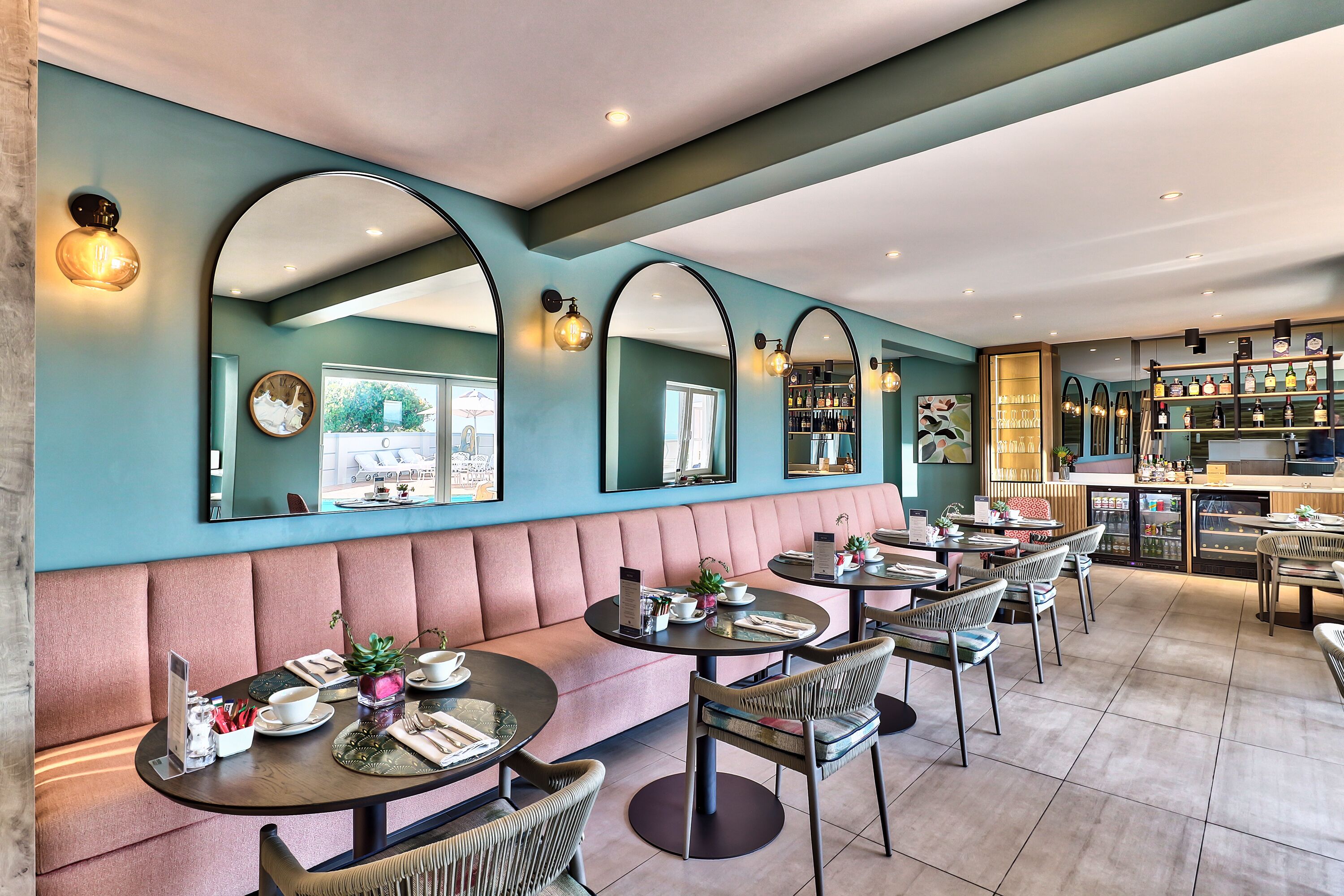 Een restaurant met een blauwgroene muur, spiegelbogen en een bar.