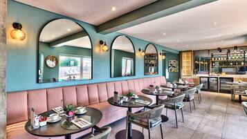 Een restaurant met een blauwgroene muur, spiegelbogen en een bar.