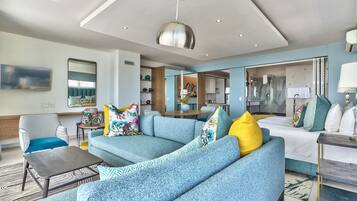 A modern hotel room with a blue sofa, a wooden coffee table, a large mirror, and a hanging pendant light.