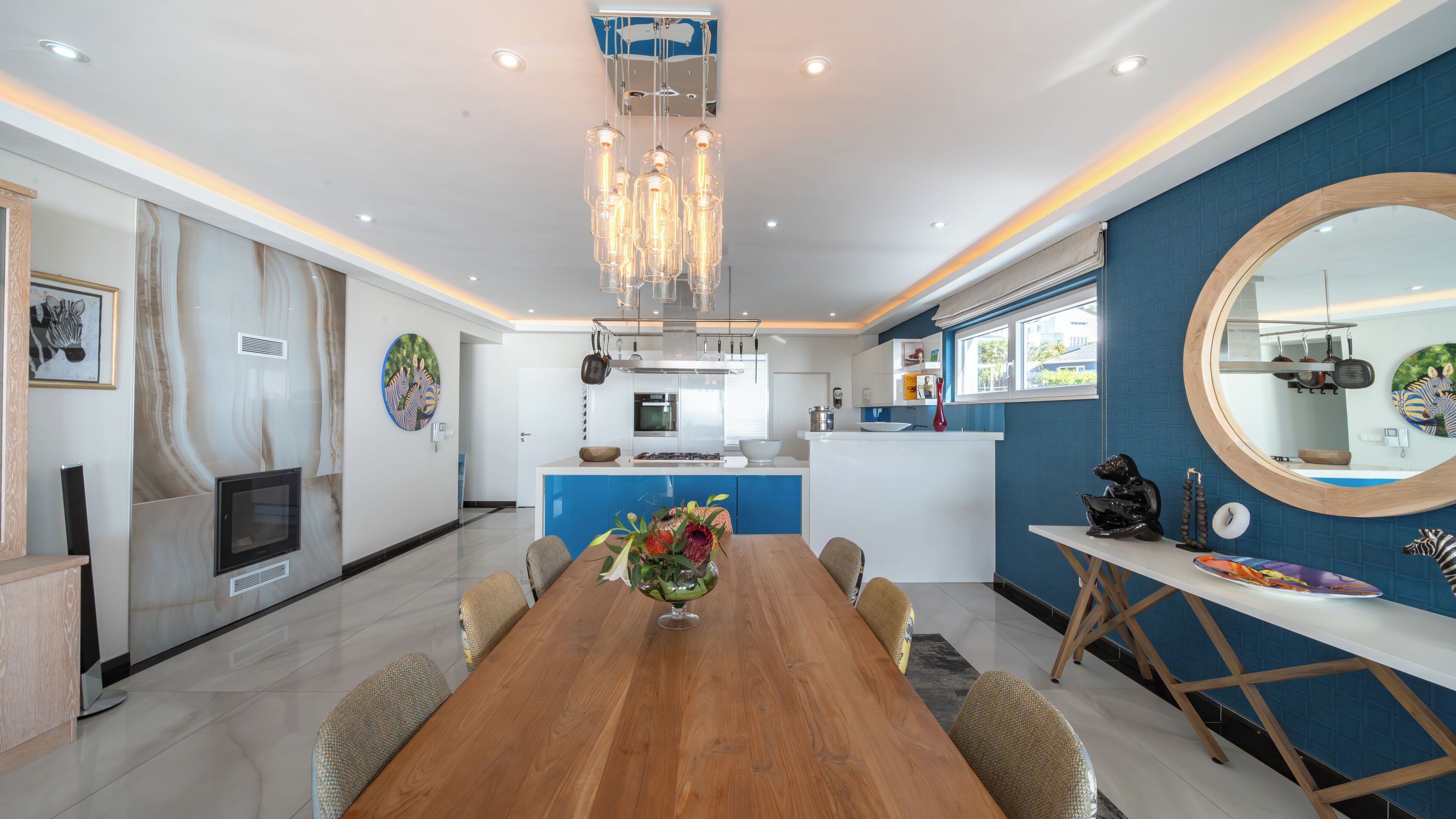 A modern kitchen with a central island, a dining area with a wooden table, and a large mirror on the wall.