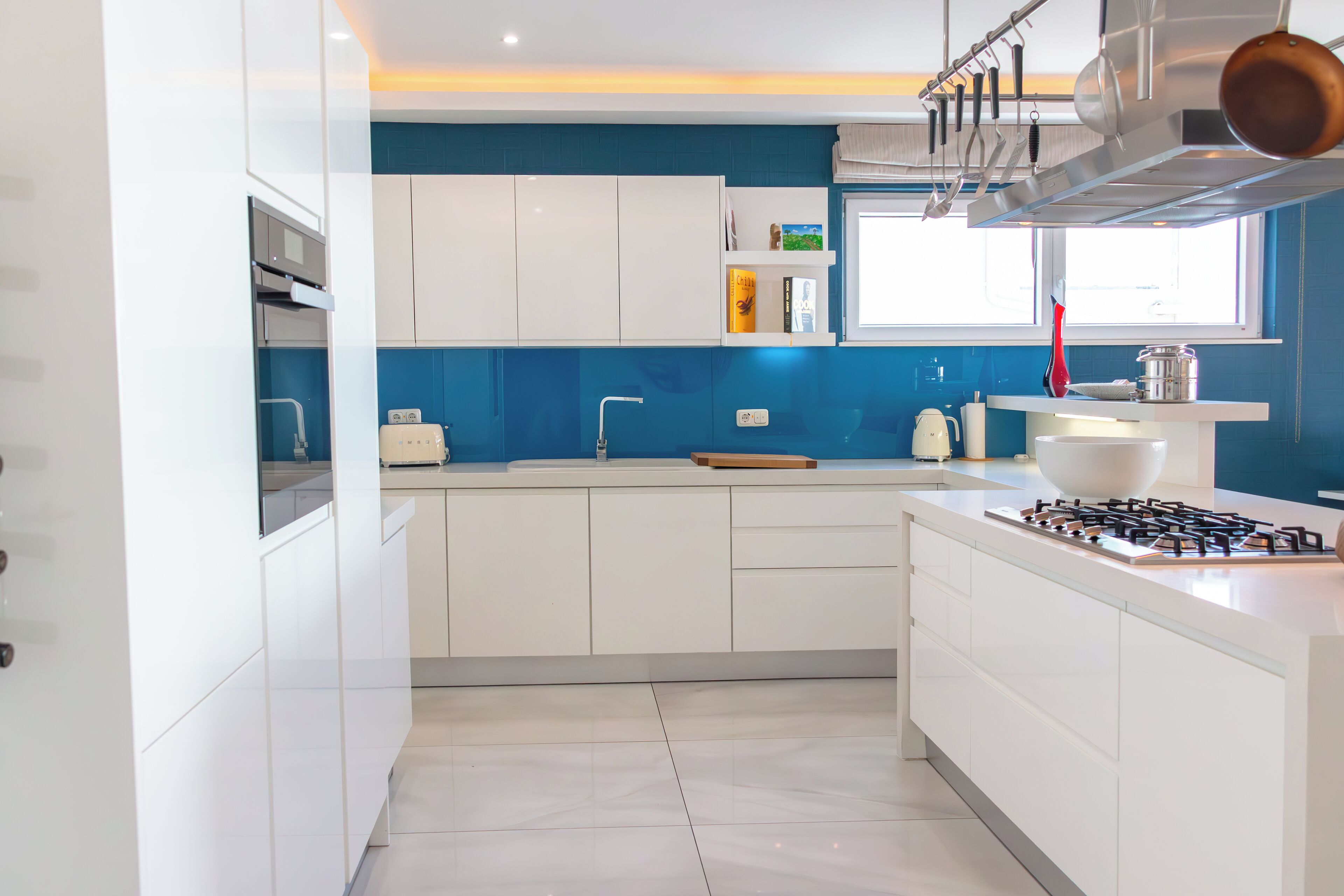 Une cuisine moderne avec des meubles blancs, une cuisinière à gaz et une fenêtre au-dessus de l’évier.