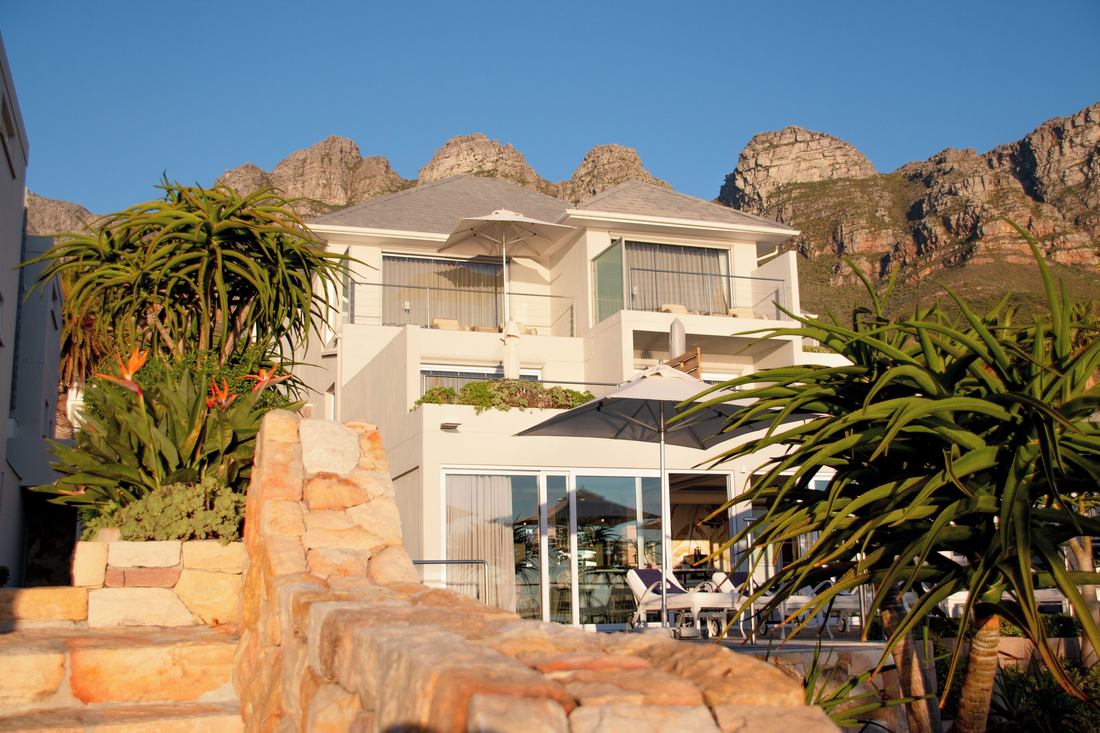 A modern two-story building with a balcony, large windows, and a view of rocky mountains.