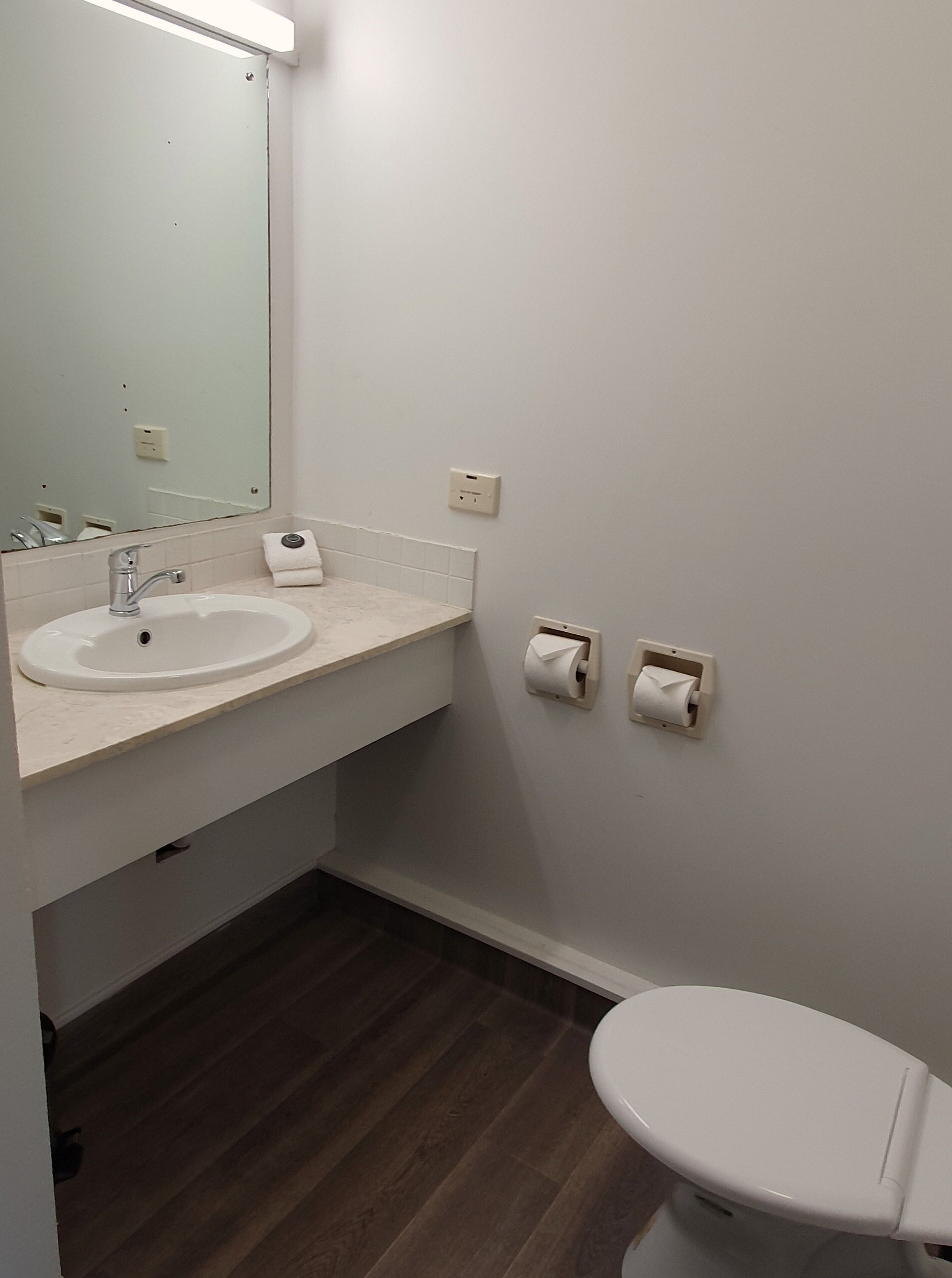 A bathroom with a white sink, mirror, and toilet. There are two paper towel dispensers on the wall.