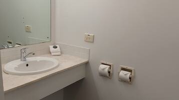 A bathroom with a white sink, mirror, and toilet. There are two paper towel dispensers on the wall.