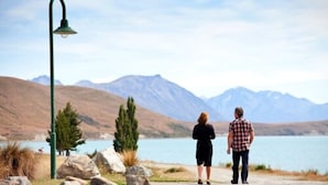 Una pareja de pie junto a un lago, con montañas al fondo.