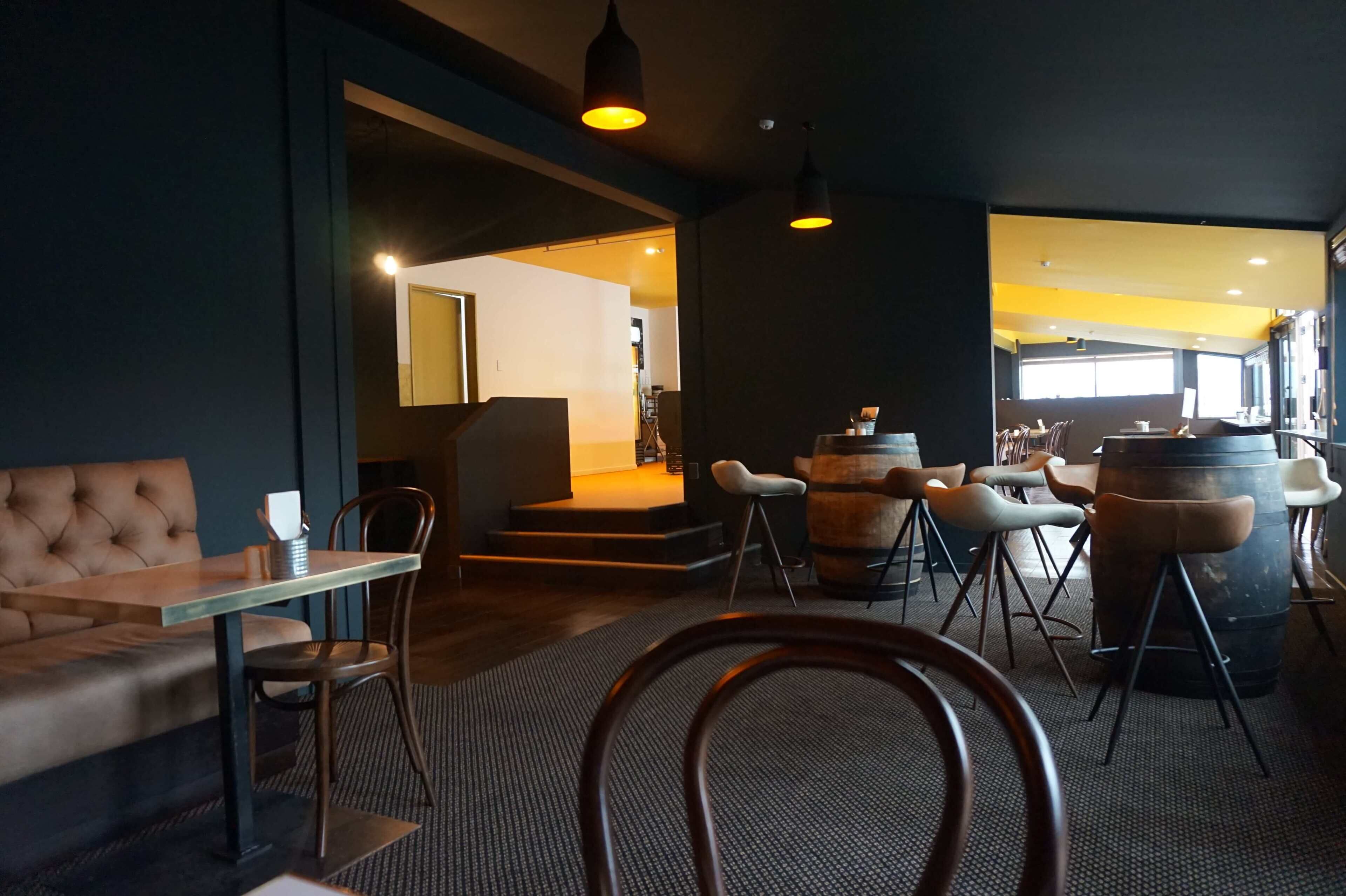 A modern interior with a sofa, dining table, chairs, and a bar area with stools and barrels.