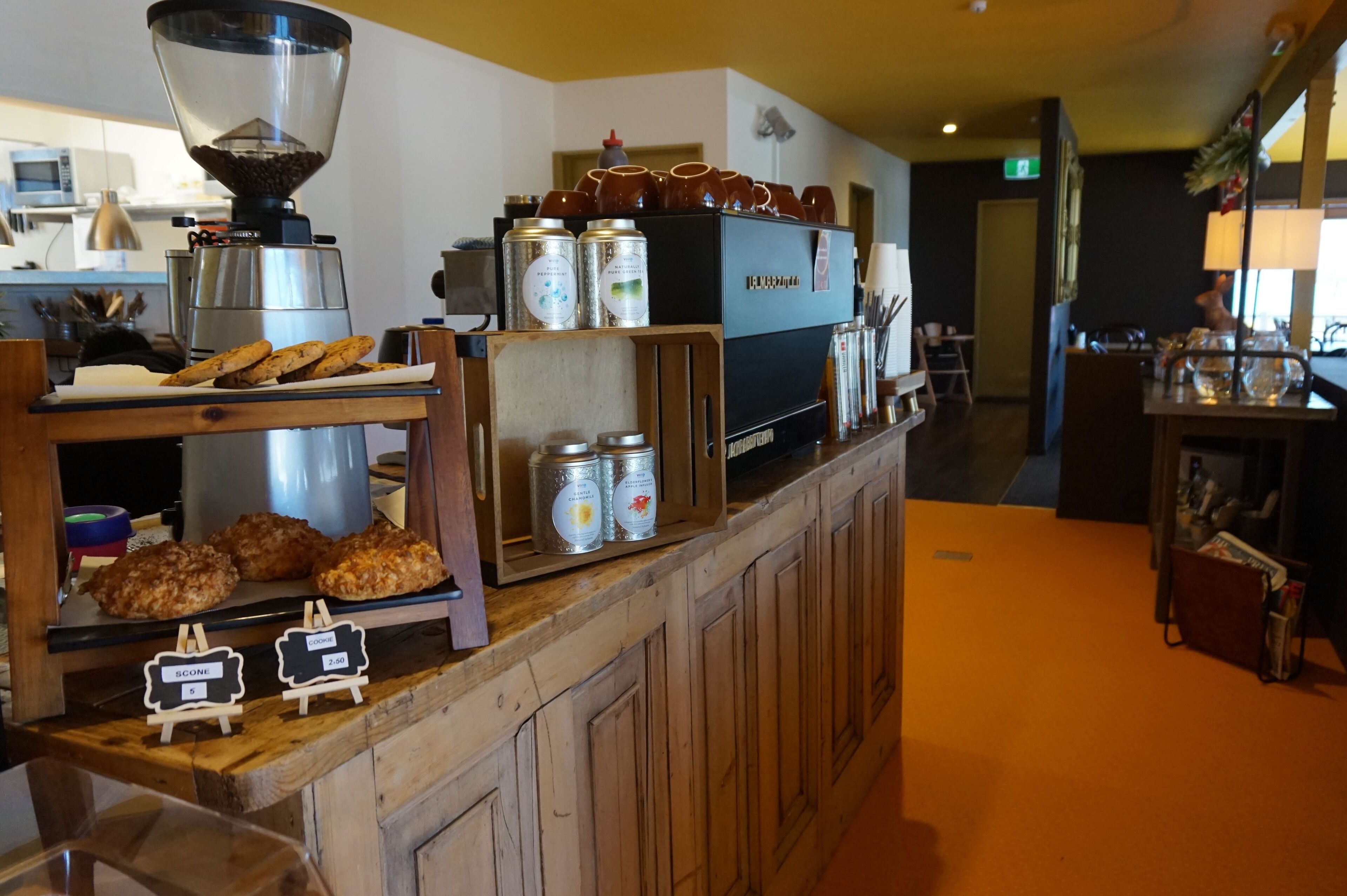 Mostrador de cafetería con molinillo de café, pasteles y bebidas enlatadas.